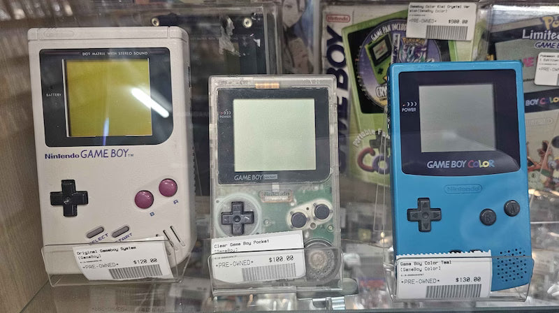 Three different Game Boy models on a shelf with more behind them.